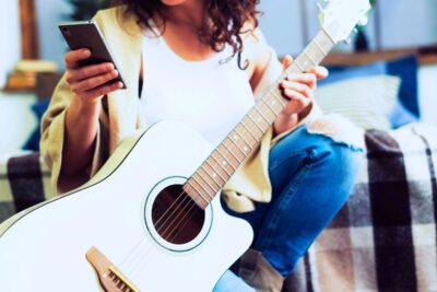 Aprende a tocar la guitarra de manera efectiva Una mujer aprende tocar la guitarra con el móvil. Foto: Freepik
